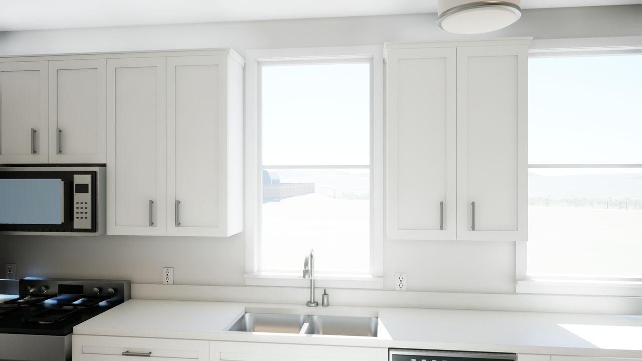 Kitchen sink beneath a window, with white upper cabinets, pale counters and a range to the left.